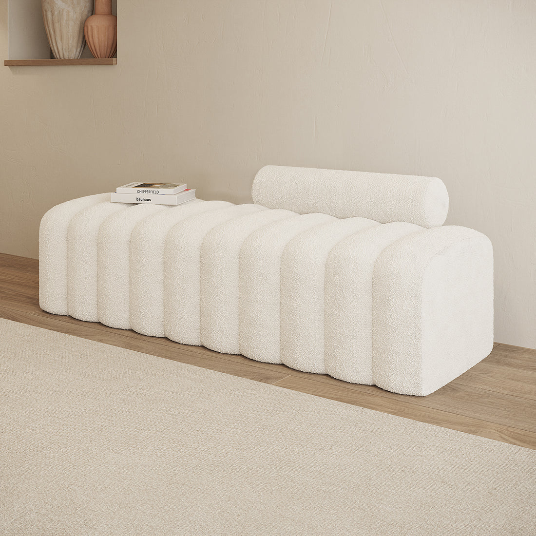 Sasa Bouclé Tufted Fabric Bench in eggshell white, featuring a sculptural design with rounded ridges and a cylindrical bolster cushion, styled with design books on a light wood floor.