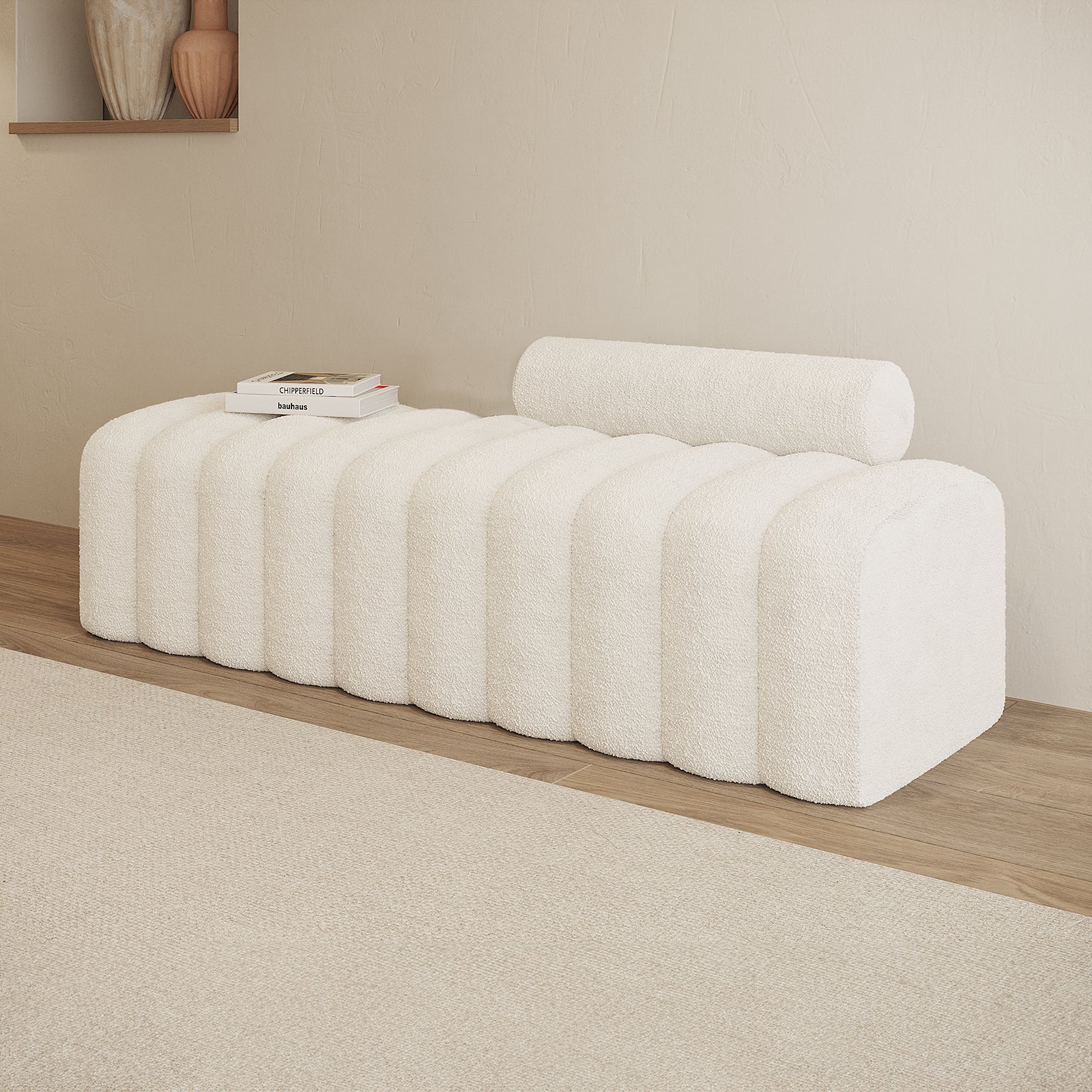Sasa Bouclé Tufted Fabric Bench in eggshell white, featuring a sculptural design with rounded ridges and a cylindrical bolster cushion, styled with design books on a light wood floor.
