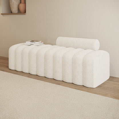 Sasa Bouclé Tufted Fabric Bench in eggshell white, featuring a sculptural design with rounded ridges and a cylindrical bolster cushion, styled with design books on a light wood floor.