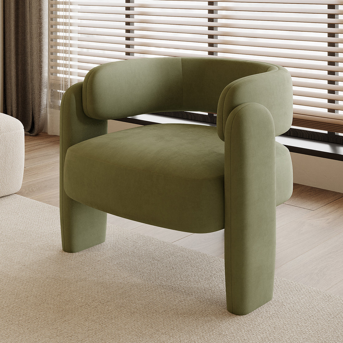 Seto Velvet Curved Occasional Accent Chair - Sage, featuring a curved backrest and thick cushioning, sits on a light rug in a bright room with wood-tone flooring and a large window.