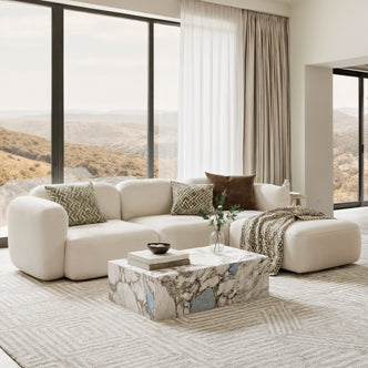 Soraya 3-Seater Velvet Sectional Sofa in Cream White, featuring a low-profile design, patterned throw pillows, and a matching ottoman, set in a bright, minimalist living room with a marble coffee table.