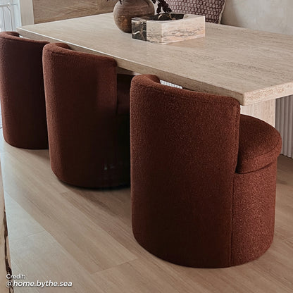 Sorra Bouclé Swivel Storage Accent Chair in Rust Brown, featuring a deep rust boucle upholstery, low barrel style with hidden storage, resting on a hardwood floor next to a minimalist table setup.