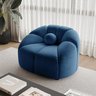Trina Single Velvet Tufted Accent Chair in Blue, featuring a plush, rounded tufted back and matching bolster cushion, set on a textured rug near sheer curtains and a coffee table.