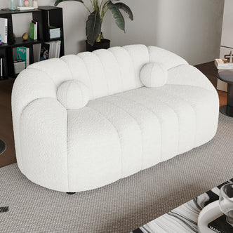 Trina 2 Seater Boucle Sofa with Pillows in Cream White, featuring a channel-stitched design, round bolsters, and set in a modern living room with a rug and plants.