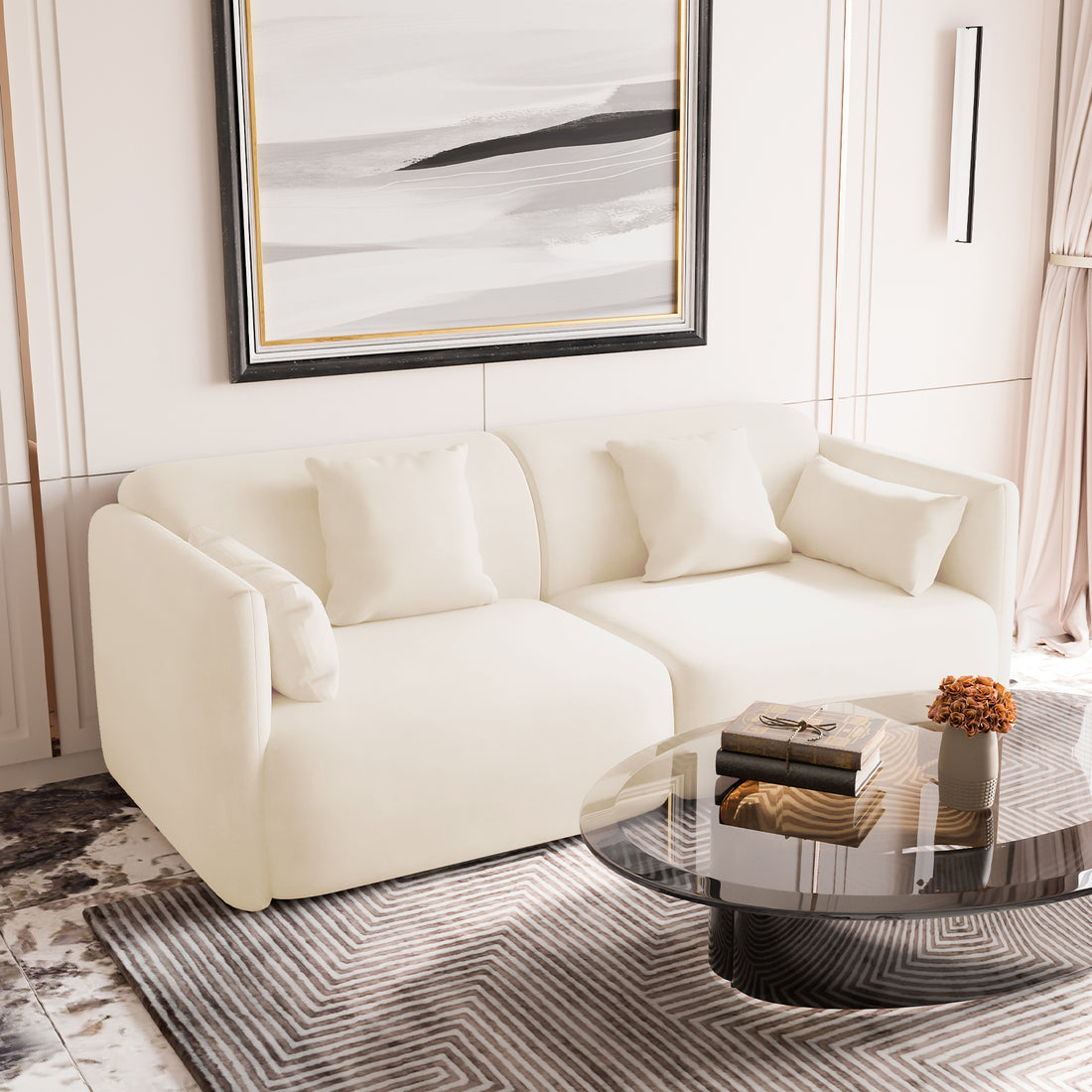 Vestalia 3-Seater Velvet Sofa in Cream White, featuring a low, curved silhouette with matching cushions, positioned in a contemporary living room setting with a glass coffee table and abstract painting above.