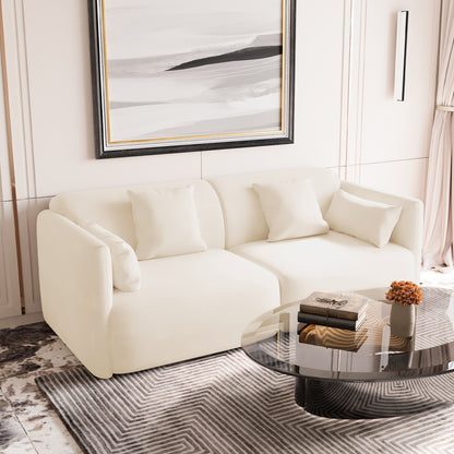 Vestalia 3-Seater Velvet Sofa in Cream White, featuring a low, curved silhouette with matching cushions, positioned in a contemporary living room setting with a glass coffee table and abstract painting above.