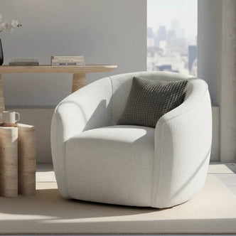 Yara Bouclé Accent Chair in Cream White, featuring softly rounded design, light-neutral upholstery, and a textured throw pillow, set on a matching rug beside a sculptural side table with a mug.