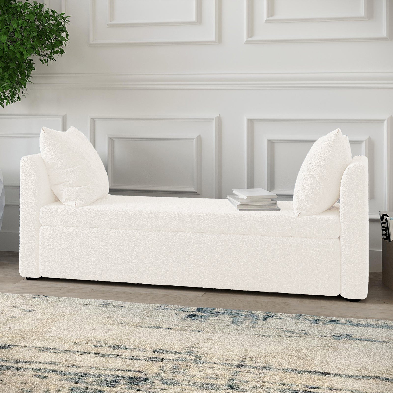 Zamira Large Boucle Storage Ottoman Bench in Cream White with bolstered arms, loose back cushions, and a book stack, set against a paneled wall, on a light rug with blue-gray accents.