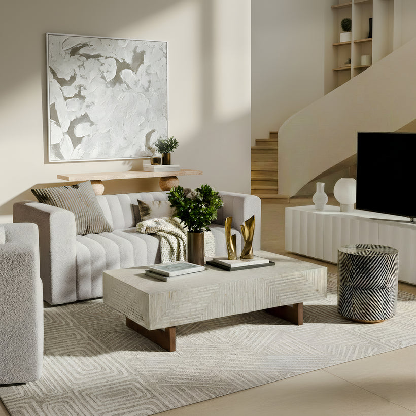 Bright, modern nursery featuring a white and natural wood crib, white changing dresser, cozy boucle armchair with matching ottoman, abstract pink and terracotta area rug, woven pendant light, botanical wall art, sheer curtains, and soft neutral décor creating a warm, calming space for a baby.