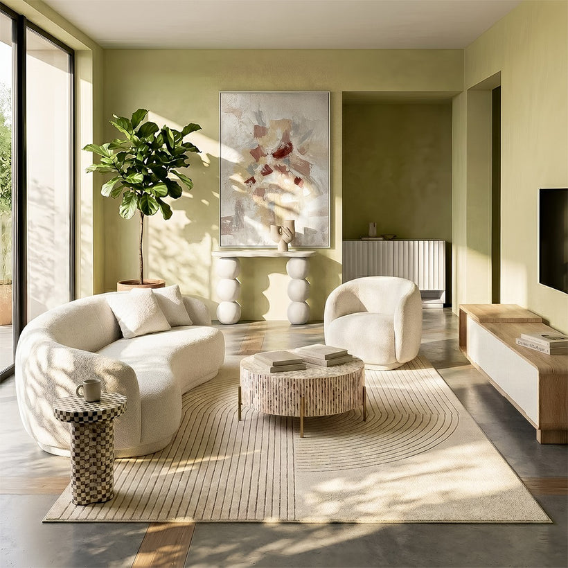 Modern dining room featuring a round light-toned dining table with six brown upholstered chairs, a sculptural pendant light overhead, a neutral patterned rug, soft sheer curtains, indoor plants, and abstract wall art, with natural light coming through large glass doors.