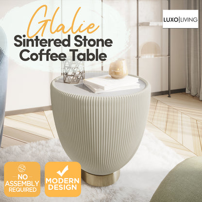 Glalie Sintered Stone Coffee Table Set in Cream White features a round, pleated tabletop on a gold-tone base, styled with décor items on a fluffy rug in a minimal living room.