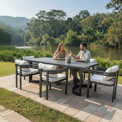 A couple enjoys drinks at a Tavari 208cm 6-Seater Curved Outdoor Dining Set in Black, surrounded by lush greenery, featuring a modern table with cushioned chairs on a scenic patio.
