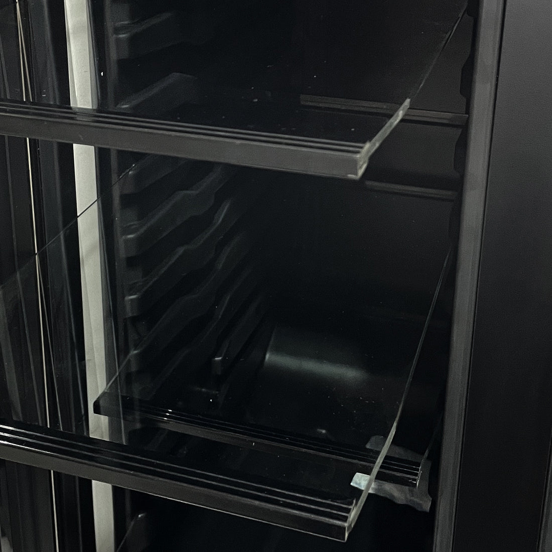 Interior view of the H140D 140L Dual Zone Wine Fridge with Chiller in Black, showcasing adjustable side rails and clear glass shelves for versatile beverage storage.