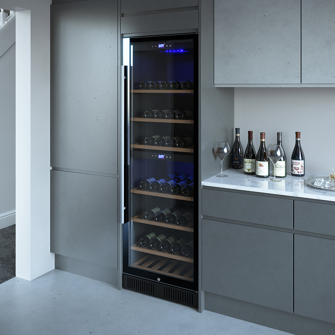 VinoVault 180 Bottle Dual Zone Built-In Wine Fridge – Stainless, featuring a glass-front with wooden shelving, surrounded by sleek grey cabinetry, stone countertop with wine bottles and glasses nearby.
