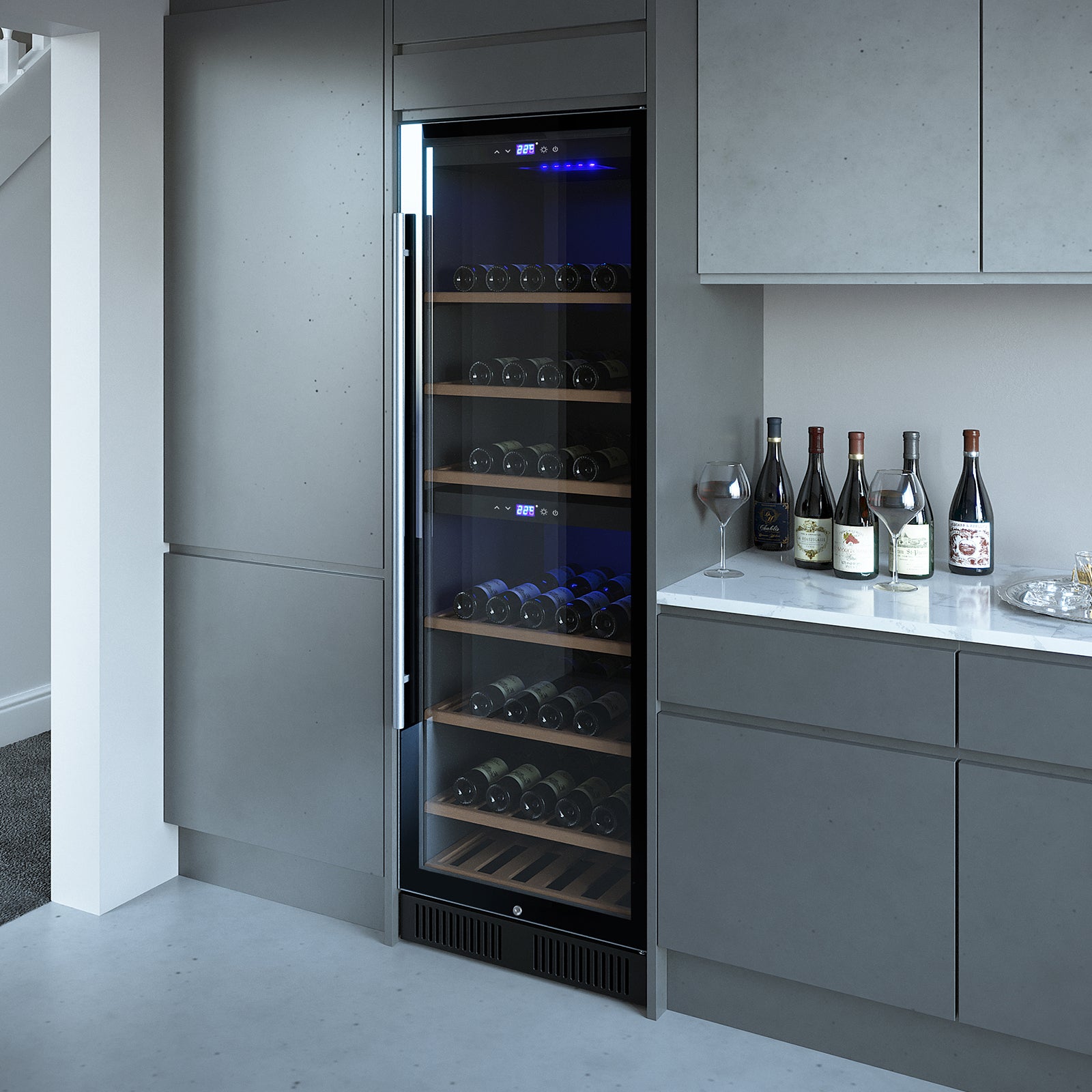 VinoVault 180 Bottle Dual Zone Built-In Wine Fridge – Stainless, featuring a glass-front with wooden shelving, surrounded by sleek grey cabinetry, stone countertop with wine bottles and glasses nearby.