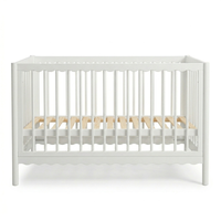 White wooden baby crib with scalloped edges and natural wood mattress slats on a white background