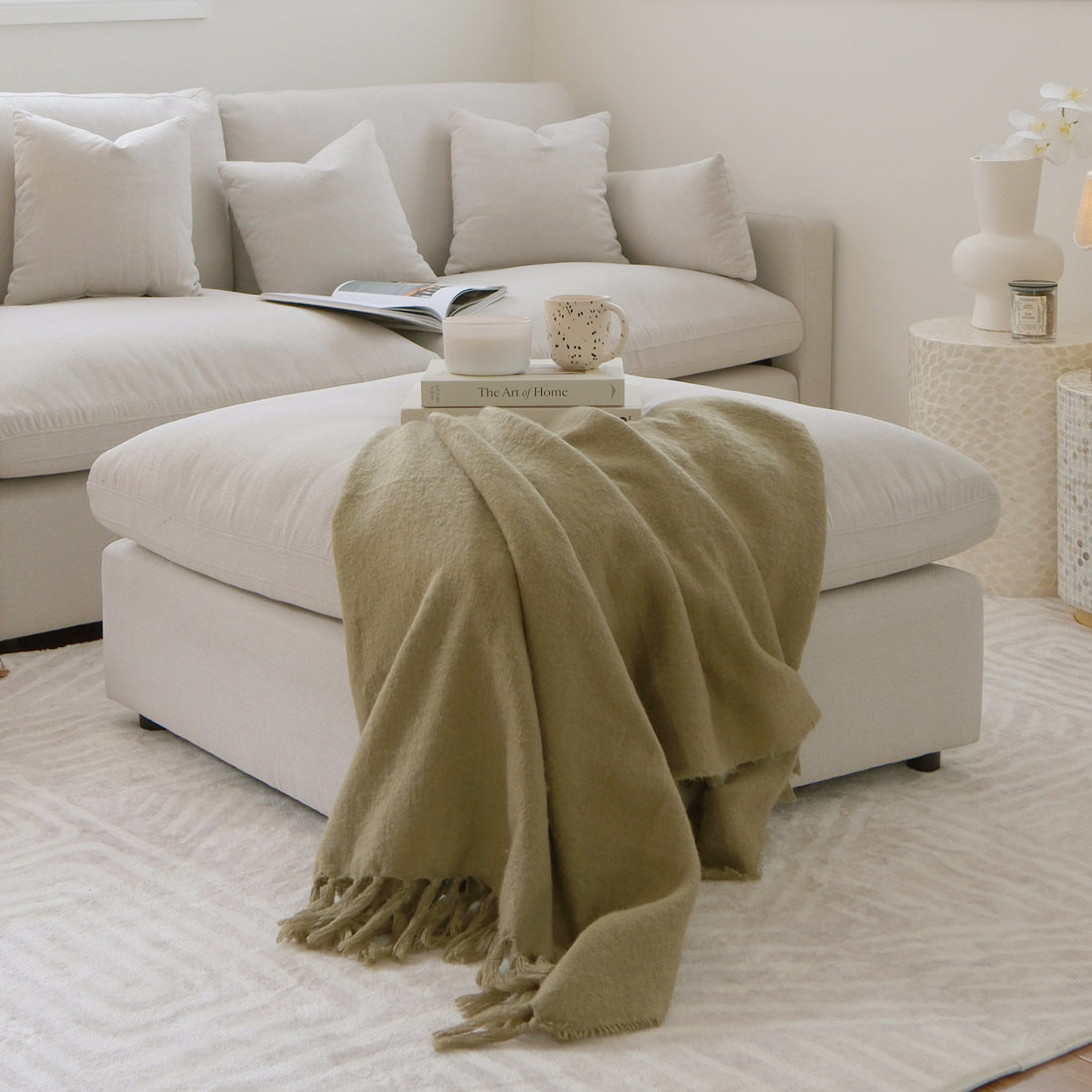 Corner of a modern sectional sofa with ottoman in a styled living room.
