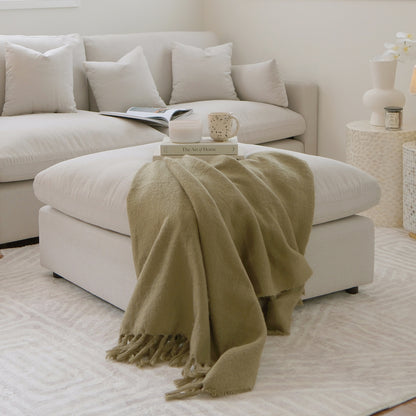Corner of a modern sectional sofa with ottoman in a styled living room.