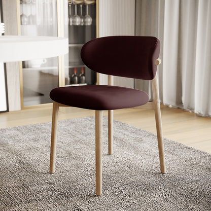 Audrey Fabric Dining Chair Set of 2 in Dark Plum, featuring a burgundy upholstered seat and backrest with light-wood legs, is showcased on a textured rug in a softly lit dining space.