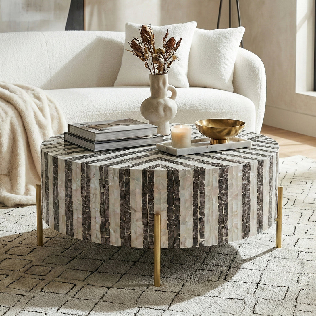 Round black and white striped coffee table styled in a living room with sofa, books, vase and decorative objects