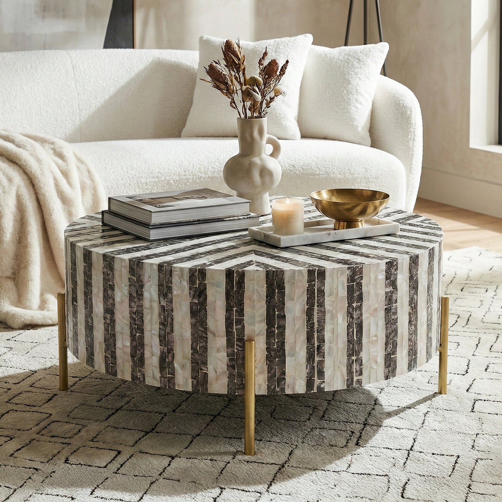 Round black and white striped coffee table styled in a living room with sofa, books, vase and decorative objects
