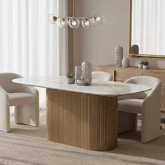 Aeris 180cm Marble Look Dining Table With Wood Base in Oak, featuring a sleek oval sintered stone top and sturdy fluted wood base, surrounded by boucle-style armchairs in a minimalist dining nook.