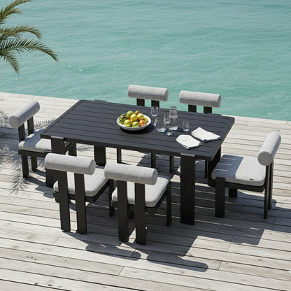 Positano 6 Seater Outdoor Dining Set in Black & Grey on a deck by turquoise water, featuring black frames, grey cushions, and a table with fruit, glasses, and napkins, hinting at a seaside setting.