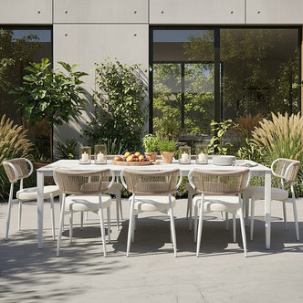 Cabria 9 Piece Sintered Stone Outdoor Dining Set with a sleek white table and eight chairs featuring woven rope backs, set on a contemporary patio with lush greenery and minimalist décor.