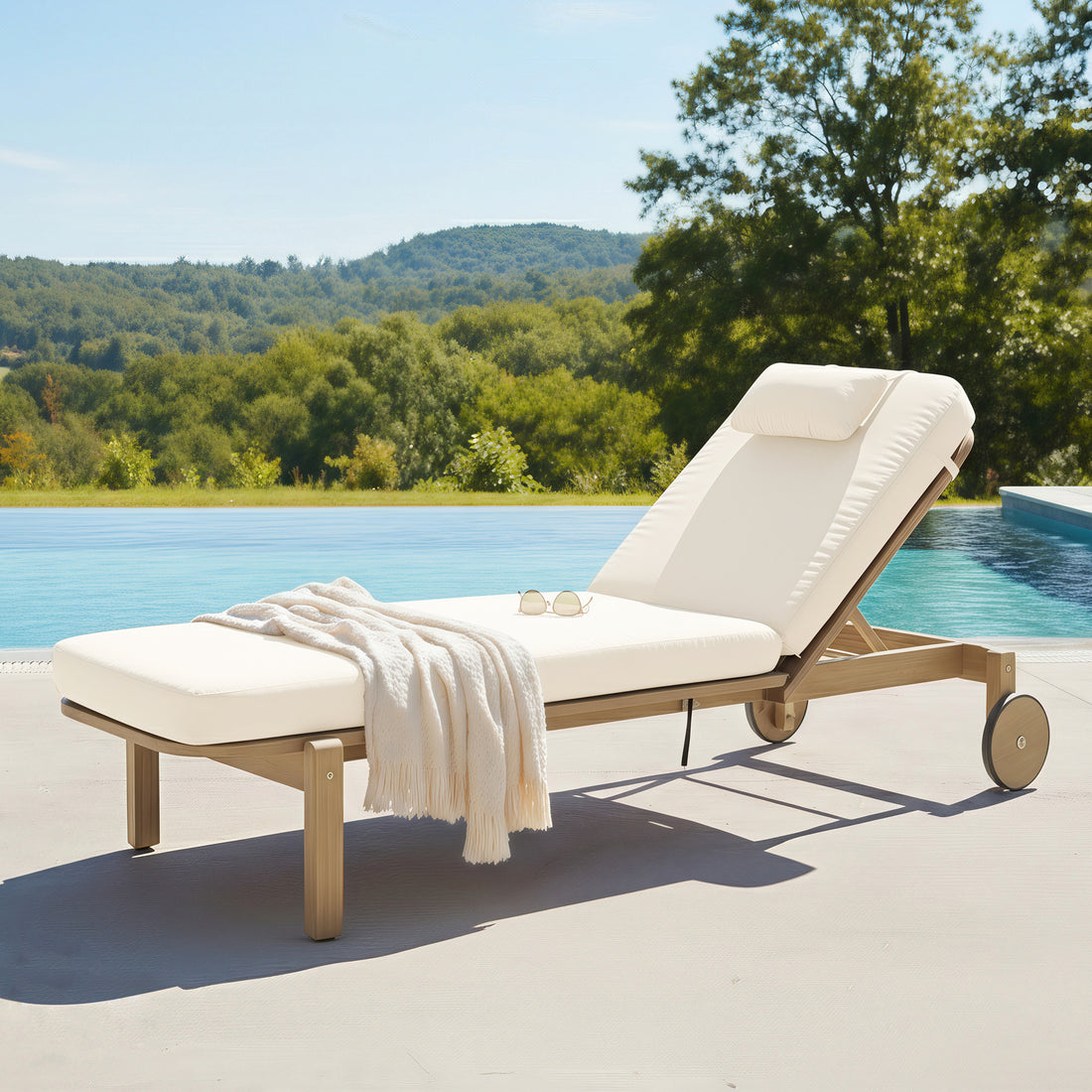 Zyra Hardwood Reclining Sun Lounger with Cushion in Cream, featuring a wooden frame, adjustable backrest, cream cushion, knit throw, and sunglasses by an infinity pool with scenic hills.