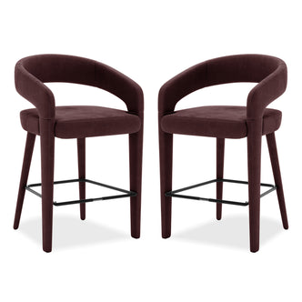 Eisha Velvet Bar Stool Set of 2 in Dark Plum features curved tubular backrests, padded seats, and tapered legs with a black metal footrest, designed for kitchen islands or home bars.