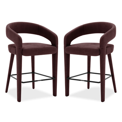 Eisha Velvet Bar Stool Set of 2 in Dark Plum features curved tubular backrests, padded seats, and tapered legs with a black metal footrest, designed for kitchen islands or home bars.