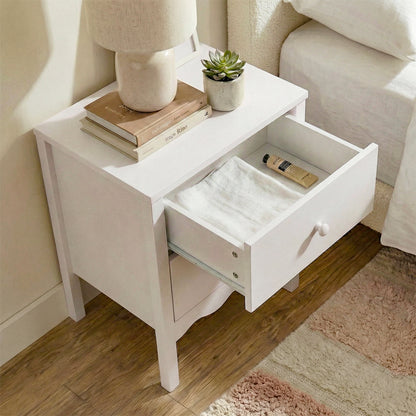 White bedside table next to bed with one drawer open, styled with books and a vase