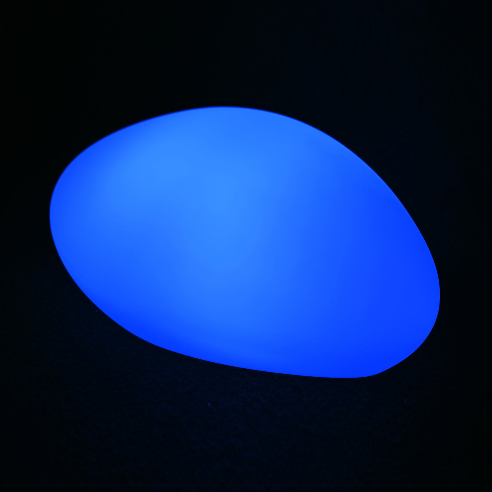 Solar Charging Outdoor LED Rock Light, a smooth, pebble-shaped object emits a blue glow on a dark surface, resembling a decorative LED lamp designed to blend into garden landscapes.