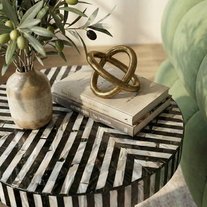 Close-up of striped table top with vase, books, and gold sculpture in a living room