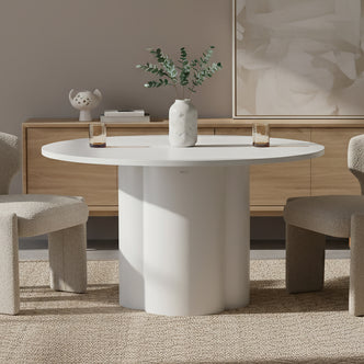 Cece 120cm Round Wooden Dining Table in White, featuring a scalloped-column base, holds a marble-effect vase with greenery. Accompanied by two boucle-upholstered chairs and amber glasses, showcasing minimalist elegance.