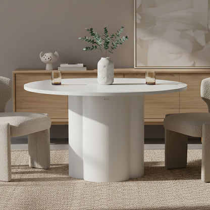 Cece 120cm Round Wooden Dining Table in White, featuring a scalloped-column base, holds a marble-effect vase with greenery. Accompanied by two boucle-upholstered chairs and amber glasses, showcasing minimalist elegance.