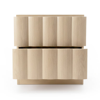 Light-colored wood nightstand with wavy drawer fronts on white background