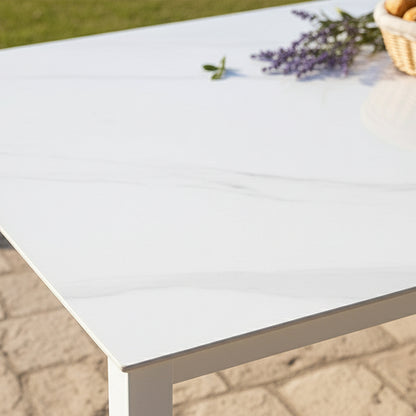 Cabria 9 Piece Sintered Stone Outdoor Dining Set showcased with a white marble-style tabletop on a patio, complemented by a wicker basket with rolls and a lavender sprig, highlighting elegance and durability.