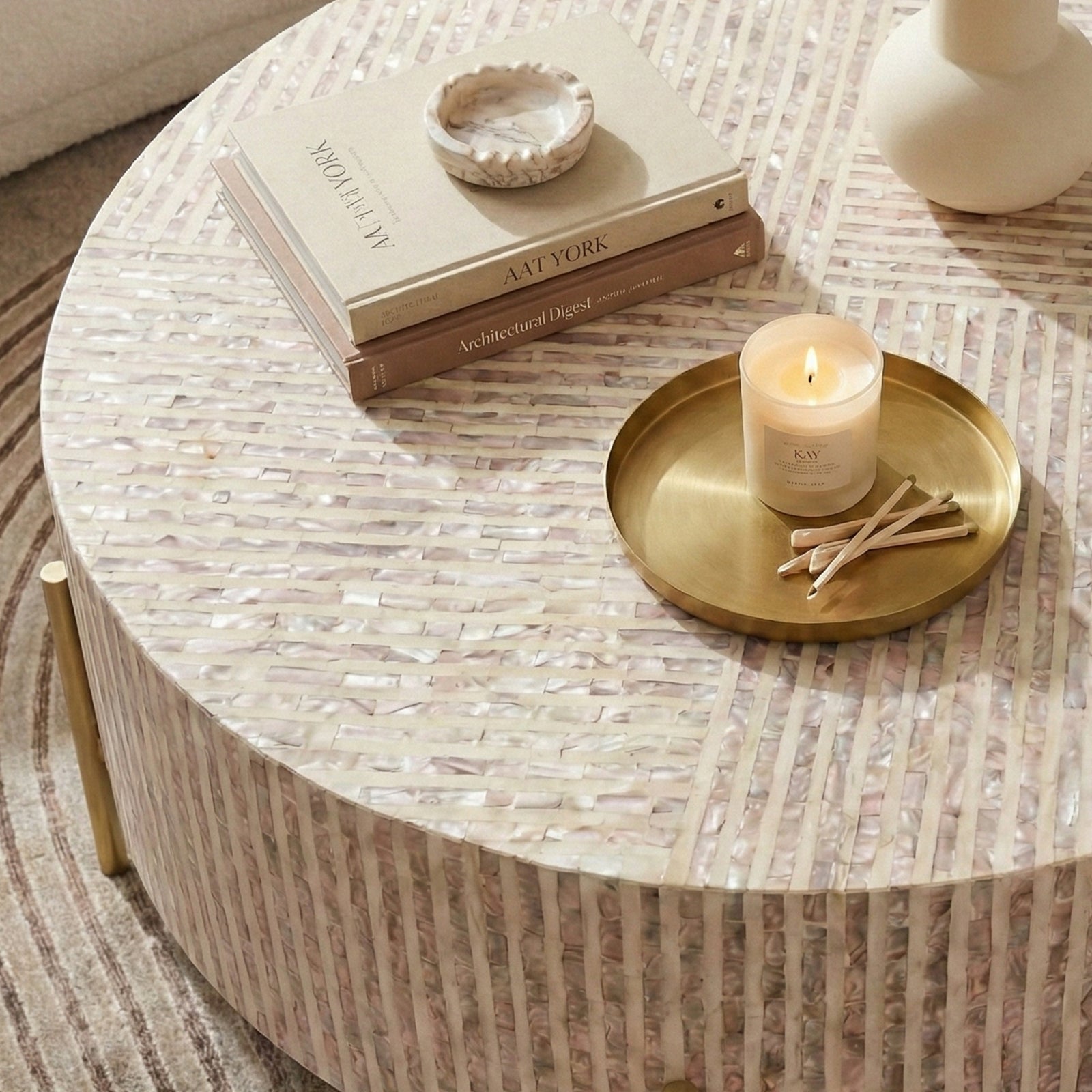 Round coffee table with iridescent surface and gold legs styled with tray, books, and vase in a room