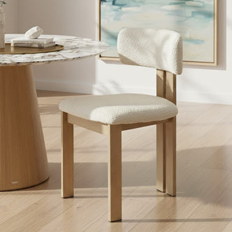 Haleo Curved Boucle Dining Chair Set of 2 in Cream White features a wooden frame with soft boucle upholstery on the seat and backrest, elegantly paired with a white marble-topped dining table.