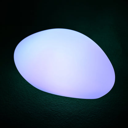 Solar Charging Outdoor LED Rock Light on a textured surface, glowing softly with color-shifting LED light, resembling a natural stone. Ideal for garden ambiance and path illumination.