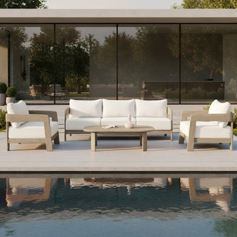 Elani 5-Seater Acacia Hardwood Outdoor Sofa Set in Cream features a wooden coffee table, plush-cushioned sofa, and two armchairs, all set beside a reflecting pool and glass doors.