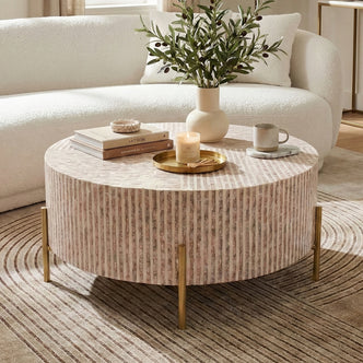 Round coffee table styled in a modern living room with sofa, rug, books, vase, and candle