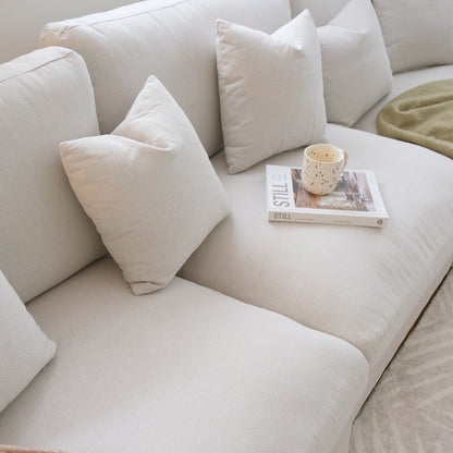Close view of a light beige sofa with pillows, book, and cup in a living room
