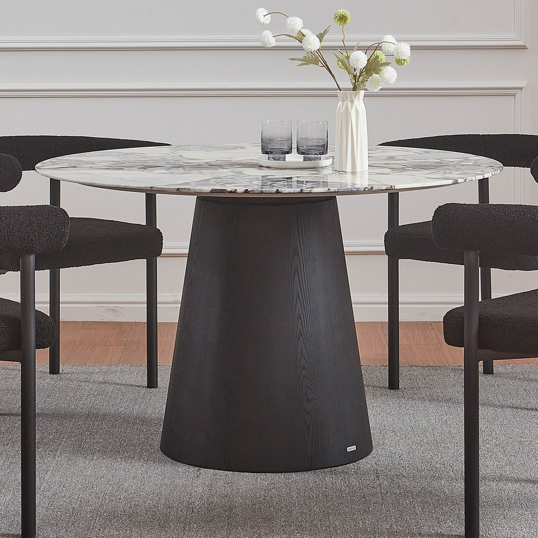 Dina 120cm Round Marble Dining Table in Blue Galaxy Black features a white-grey marble top with veining and a black tapered pedestal, surrounded by black boucle-style chairs with metal legs.