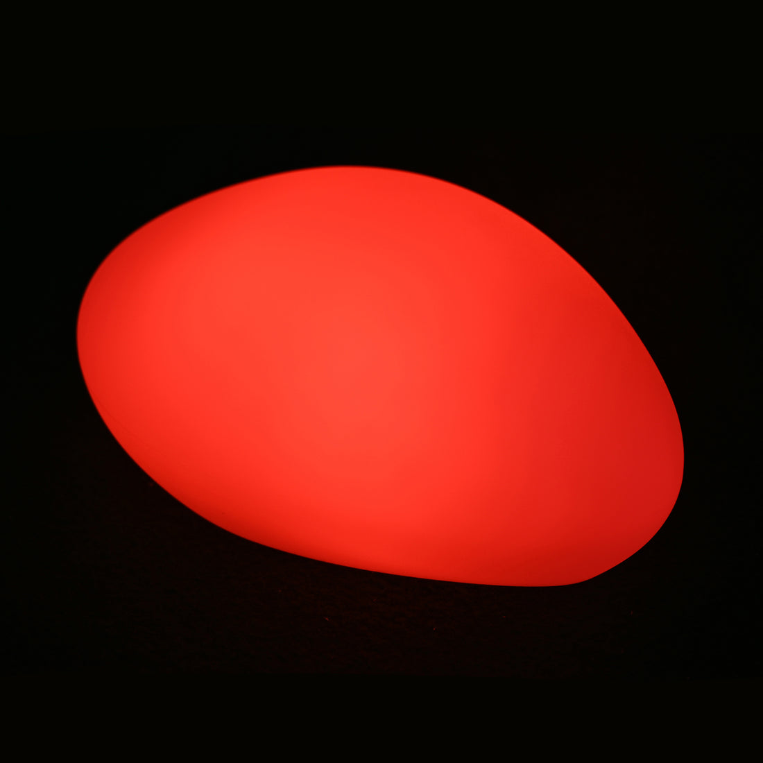 The Solar Charging Outdoor LED Rock Light, resembling a glowing red pebble or egg, illuminates against a black background, highlighting its smooth, oval design and cordless ambiance.