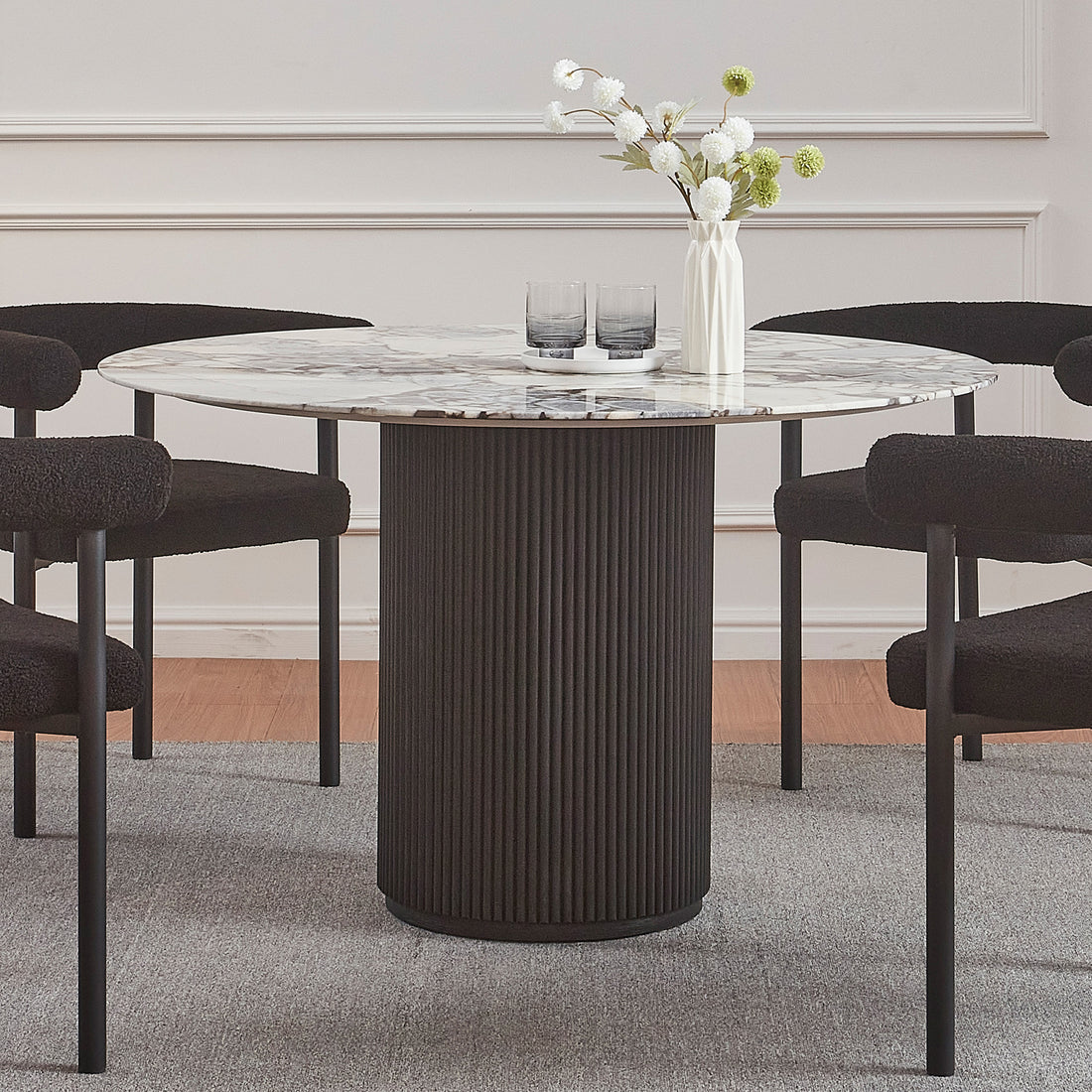 Gracie 120cm Round Marble Dining Table in Black features a marble top on a fluted black base, surrounded by four black chairs. A vase and tray adorn the tabletop.