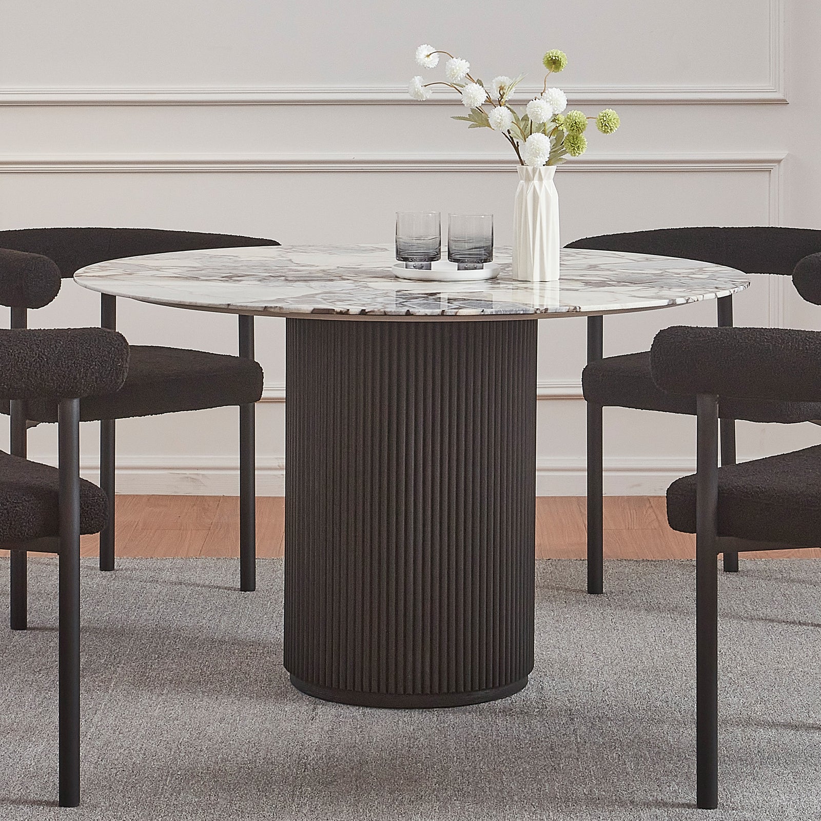 Gracie 120cm Round Marble Dining Table in Black features a marble top on a fluted black base, surrounded by four black chairs. A vase and tray adorn the tabletop.