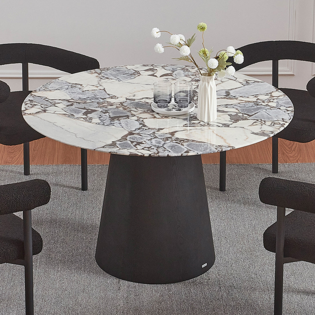Dina 120cm Round Marble Dining Table in Blue Galaxy Black, featuring a white-and-gray marble top and a solid black pedestal base, surrounded by four black chairs on a neutral rug.
