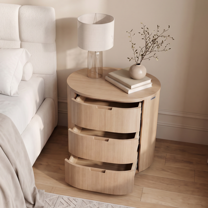 Light wood bedside table with drawers styled next to a bed in a bright bedroom